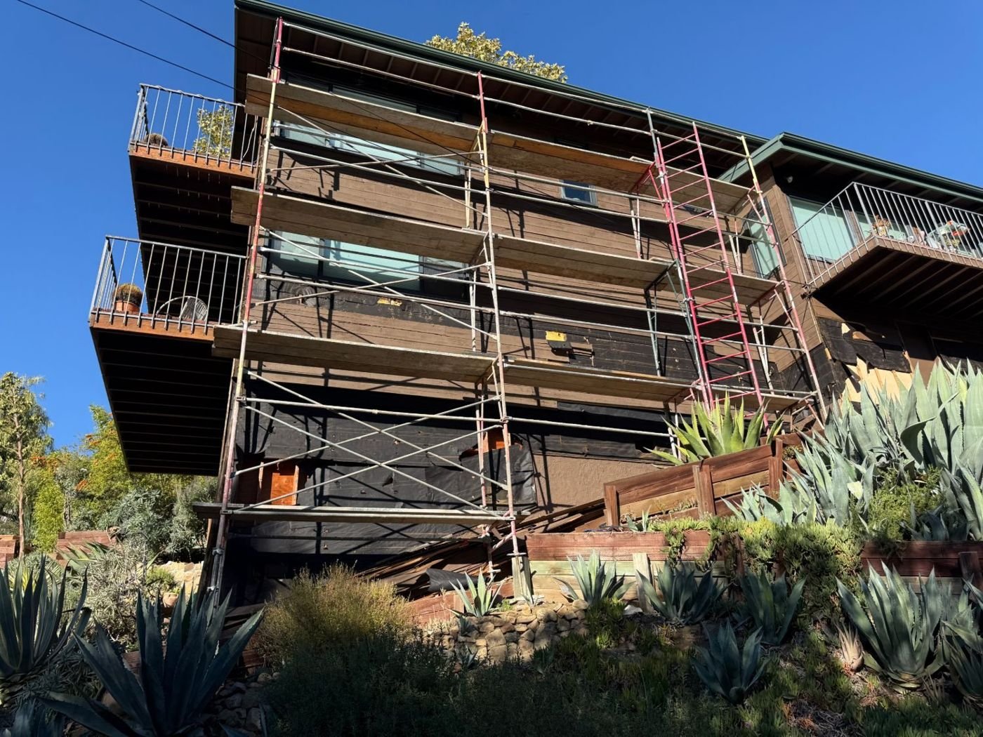 Weathered wood siding on a hillside house before replacement