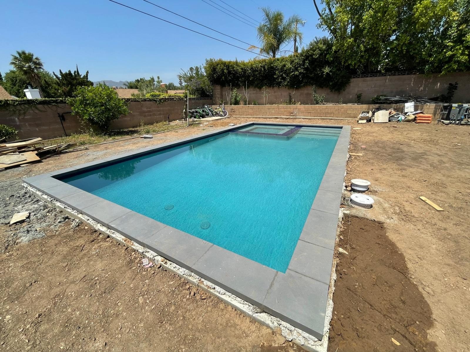 Newly constructed gunite pool with dark coping before decking — Right Image Builders