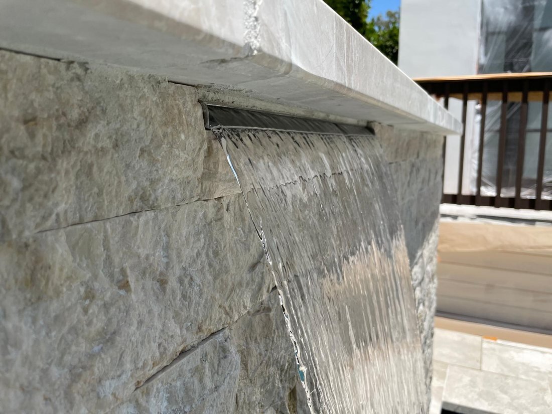Stone sheer-descent water feature spilling into a new pool — Right Image Builders